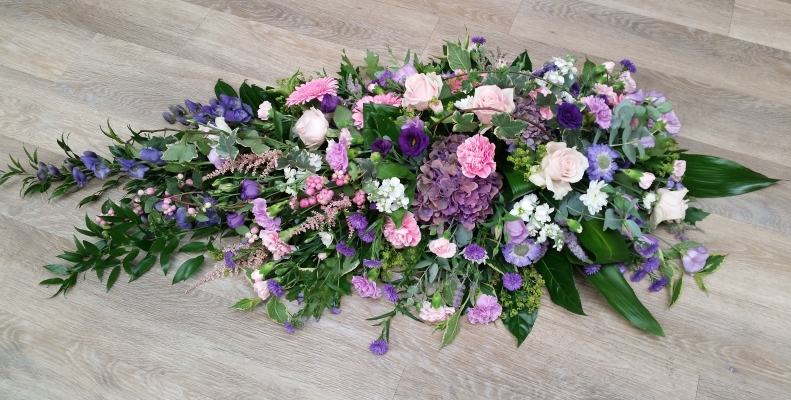 Country style pink, purple and lilac flower and foliage single ended funeral coffin spray 