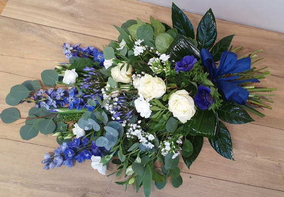Funeral hand-tied sheaf with blue and white blooms, ivory roses, blue delphinium, blue agapanthus, double white lisianthus, anemones and various foliages in glossy green and silver grey.
