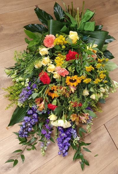 Hand-tied funeral sheaf with sunflowers, purple delphiniums and other flowers in citrus yellow, red and orange