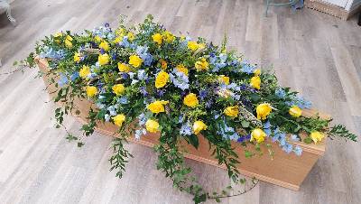 Country yellow rose and blue delphinium flower double ended funeral coffin spray, with foliage including wheat and trails