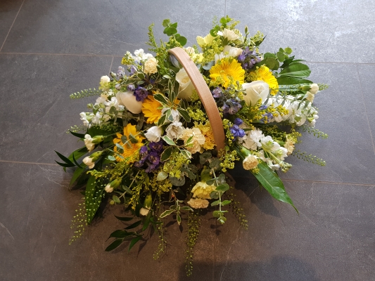A country-style trug with blue delphinium, scented white stocks, golden yellow germini, ivory roses, and solidago. 