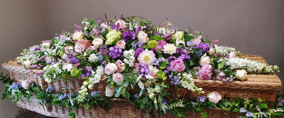 A double-ended  coffin spray featuring a combination of pale pink roses, lavender stocks, purple lisianthus, white snapdragons, and lush greenery.