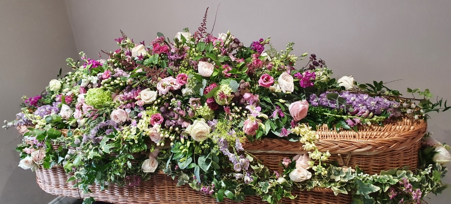 A naturally beautiful coffin spray with a mix of pink roses, deep pink lisianthus, deep pink snapdragons, green viburnum, deep lilac delphinium, pretty pink garden roses, scented stocks and lush greenery.
