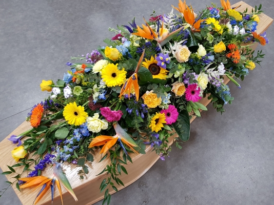 This special double-ended coffin spray features a mix of sunflowers, Birds of Paradise, yellow roses, orange and yellow gerberas, purple irises, blue delphiniums, pink spray roses, cerise germini and peach garden roses