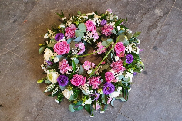 Funeral wreath tribute with vibrant pink roses, soft white roses and purple lisianthus with a collection of complimenting flowers and foliage. 