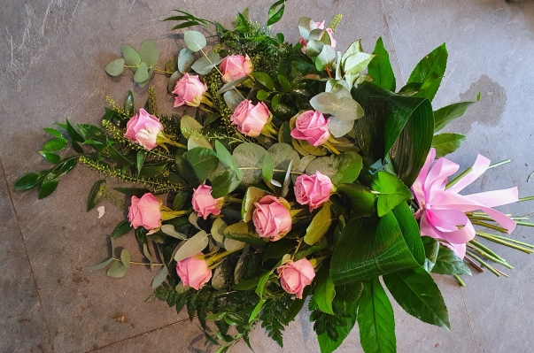 A beautiful hand-tied funeral sheaf of 12 premium pink roses with an abundance of gorgeous foliage.