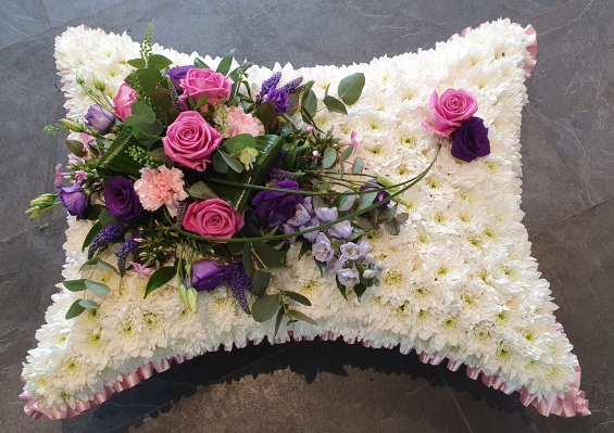 Pillow shaped tribute with white chrysanthemum based and a delicate spray of pink roses and lilac blooms, finished with a soft baby pink ribbon edge and optional name ribbon.