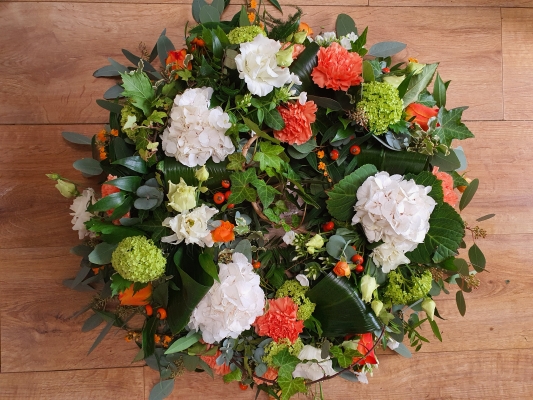 Funeral wreath tribute with orange carnations, roses and rustic berries give this wreath an Autumn feel, lightened by the white hydrangea and accents of lime green.