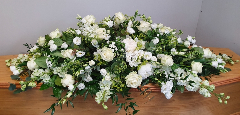 Coffin spray with a pure blend of white roses, white lisianthus, white delphiniums, white alstroemeria, white stocks, white bouvardia and lush greenery.