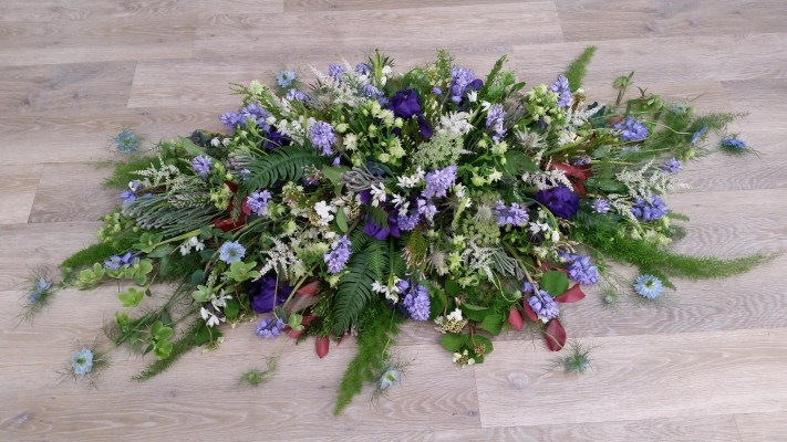 Coffin spray with a seasonal woodland style mix including snowdrops, bluebells, astilbe, lisianthus, astrantia, hellebores, and nigella, finished with mixed foliage.