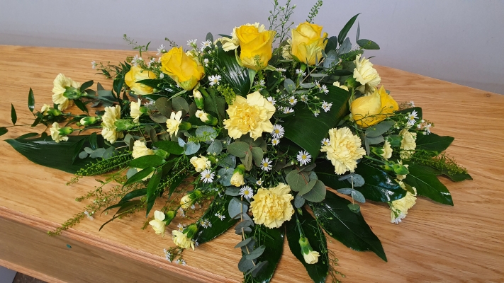 A pretty all yellow single ended spray of vibrant yellow roses, yellow carnations and spray carnations with an infill of white daisies and glossy mixed foliage.