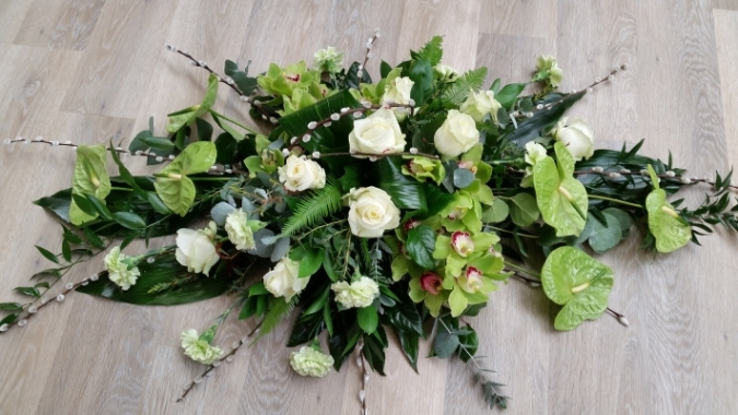 A contemporary double ended funeral coffin spray with green orchids and anthuriums, white roses and modern foliage