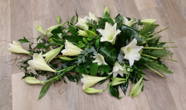White flower and foliage single ended funeral coffin spray with longi lilies and stems at the end to look like a hand-tied arrangement