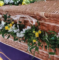 Country style foliage coffin garland including spray roses and fragranced flowers threaded around casket 