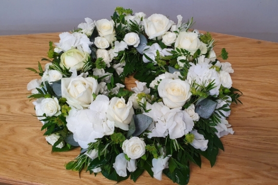 Funeral wreath ivory roses and spray roses, with pure white hydrangea and sweet scented freesia or sweet peas when in season.