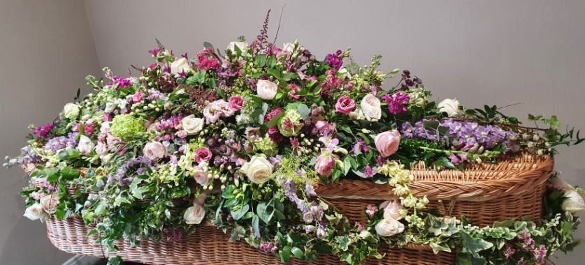 A naturally beautiful coffin spray with a mix of pink roses, deep pink lisianthus, deep pink snapdragons, green viburnum, deep lilac delphinium, pretty pink garden roses, scented stocks and lush greenery.