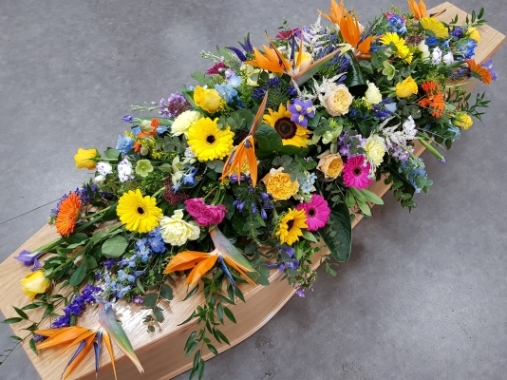 This special double-ended coffin spray features a mix of sunflowers, Birds of Paradise, yellow roses, orange and yellow gerberas, purple irises, blue delphiniums, pink spray roses, cerise germini and peach garden roses