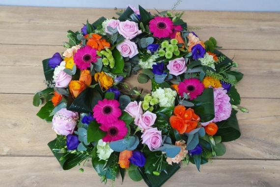 Wreath tribute with cerise gerberas, pink and orange roses, purple lisianthus and other seasonal flowers, finished with fresh foliage to complement.