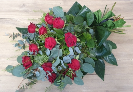 Funeral sheaf of 12 red roses with beautiful green and silver-grey foliage.
