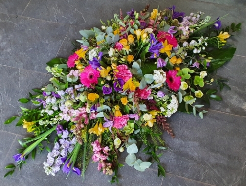 Springtime Coffin Spray with a mix of pink gerberas, yellow freesias, pink snapdragons, purple irises, green hellebore, lilac delphinium, daffodils, pink stocks and white phlox with lush greenery,
