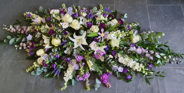 A double-ended coffin spray featuring a combination of white roses, purple lisianthus, white lilies, lavender stocks and lush greenery.