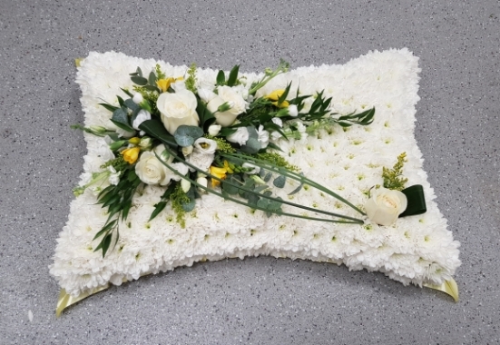 A pillow shaped tribute based in pure white chrysanthemums, with an elegant white rose and yellow freesia spray and complementary foliage.